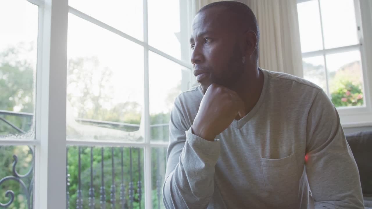 Stressed african american man looking out of the window while sitting on the couch at home