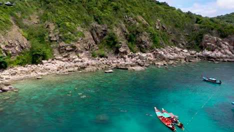 drone aerial shot of rocky bay with longtails and coral reef on koh tao, thailand