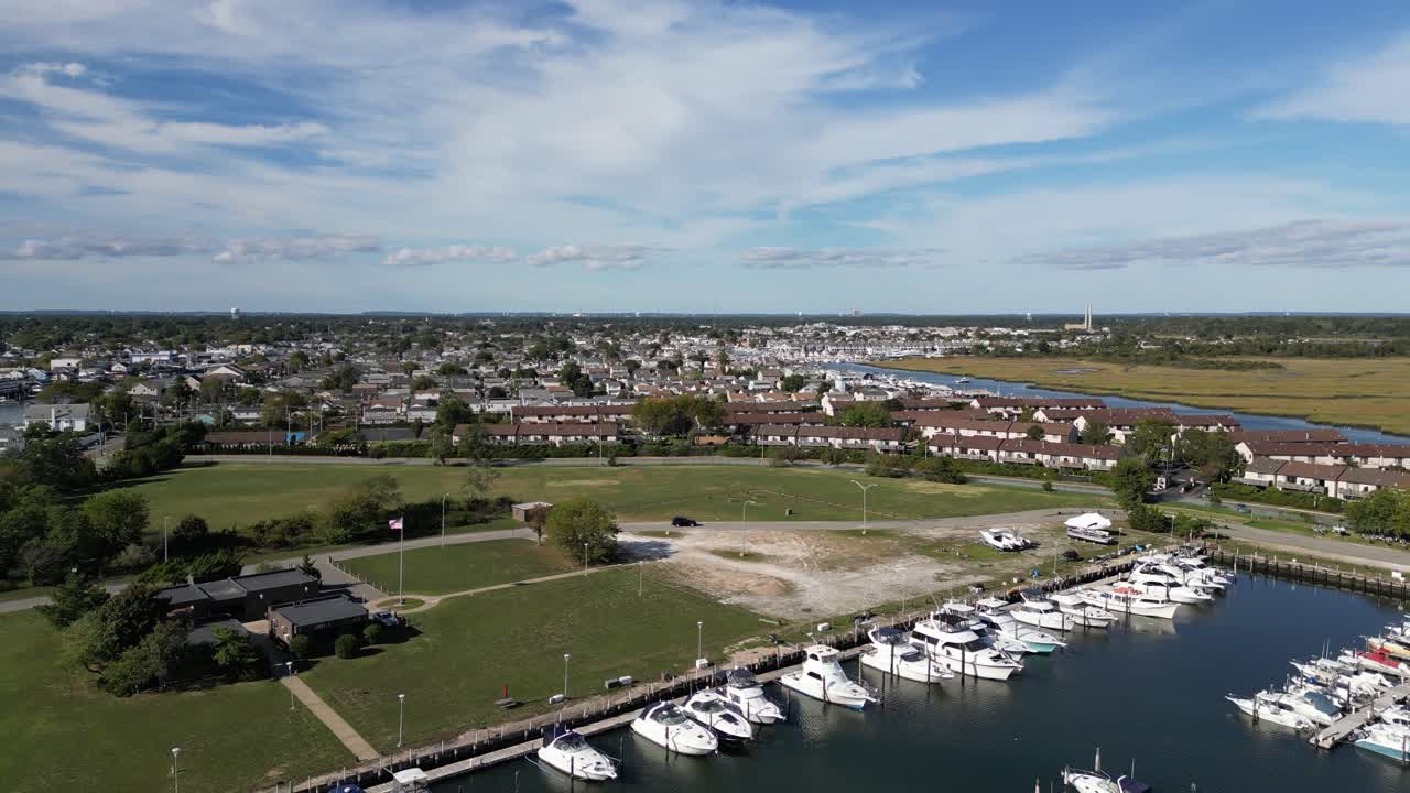 Smukt luftfoto flyvende over en lille marina fyldt med både og et boligområde med en blå himmel og spredte skyer i baggrunden på en solrig dag i New York.