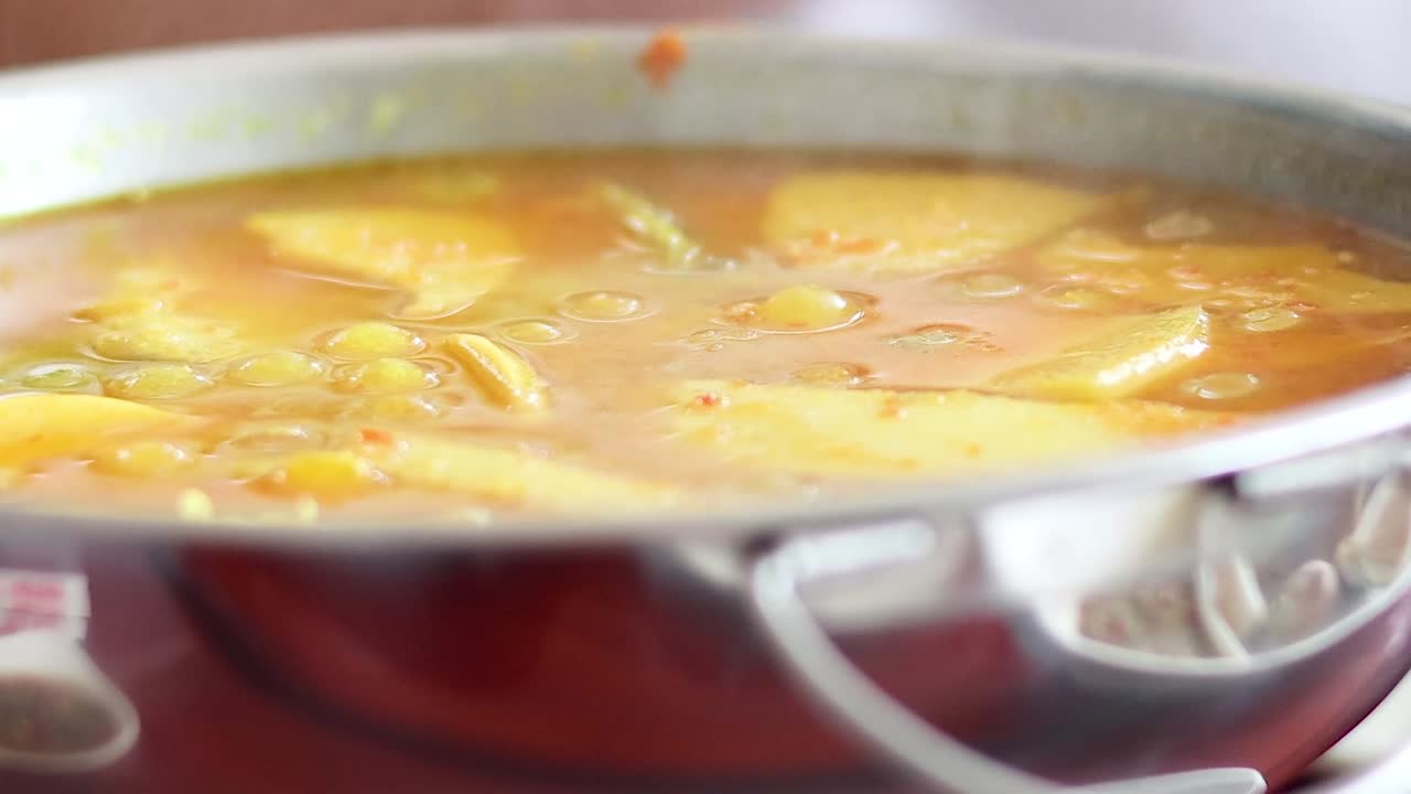 Un primo piano di zuppa di curry giallo piccante e bollente servita in una pentola di metallo.