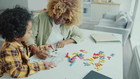 black mother teaching kid to draw with marker pen on paper at home