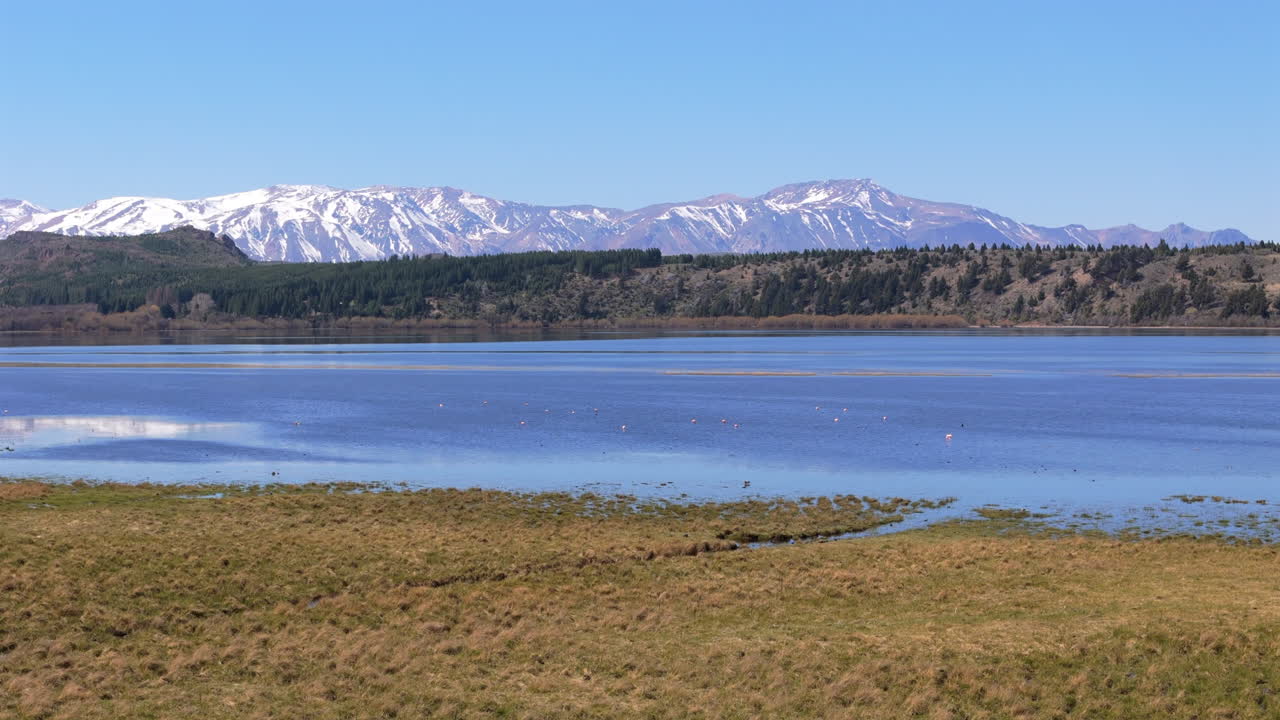 Idyllic blue lake with mountains at the horizon, aerial view zoom-in