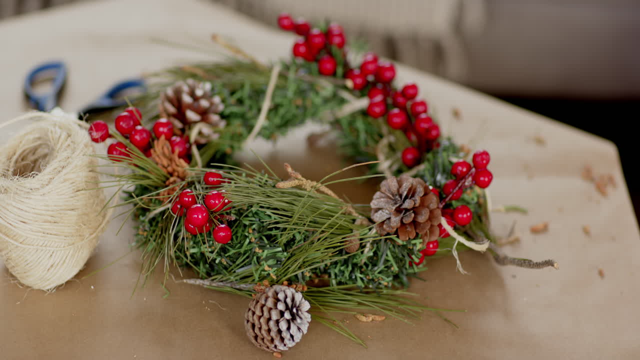 Festive Christmas wreath with pinecones and berries on crafting table