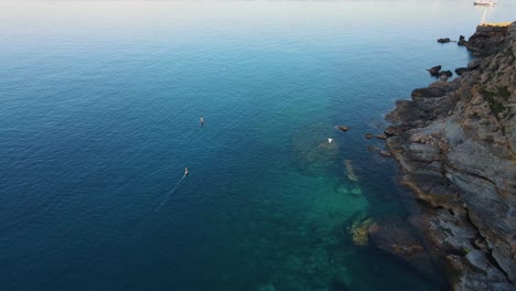 Aerial-landscape-view-of-people-surfing-with-an-electric-board-in-Cala-Escondida,-Ibiza,-Spain