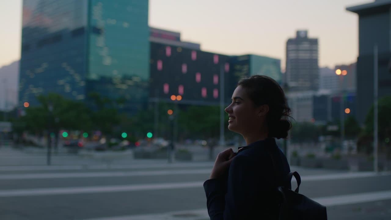 joven feliz mujer de negocios pasante esperando en la calle de la ciudad urbana buscando pensamiento pensativo disfrutando de la noche tranquila con mochila