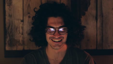 exuberant man with curly hair with glasses laughing cheerfully in warm light