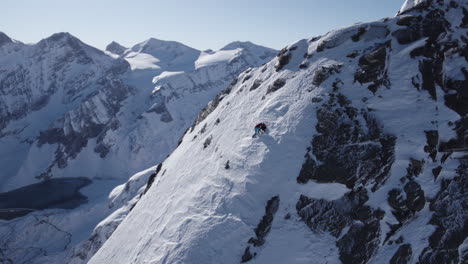 Drone-shot-of-Mountain-Climber-hanging-on-steep-snowy-mountain-during-sunlight