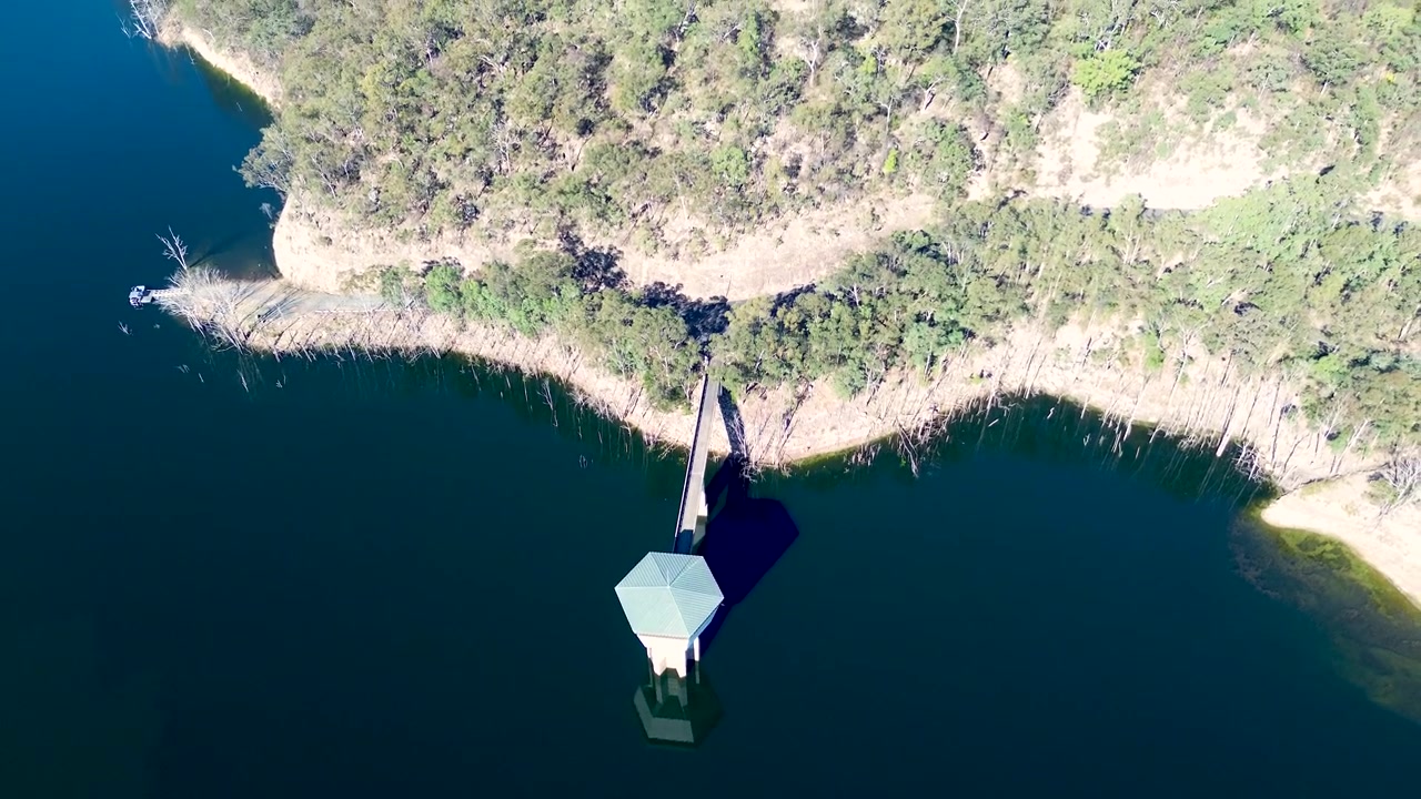 Drone aerial landscape of an intake tower and access walkway bridge surrounded by a bushland forest headland at Mangrove Creek Dam reservoir near Kulnura on the Central Coast Australia infrastructure