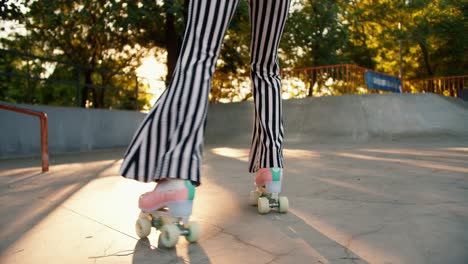 close-up shot: a girl in striped pants rides on pink roller skates in a skate park on a concrete surface. outdoor activities in summer