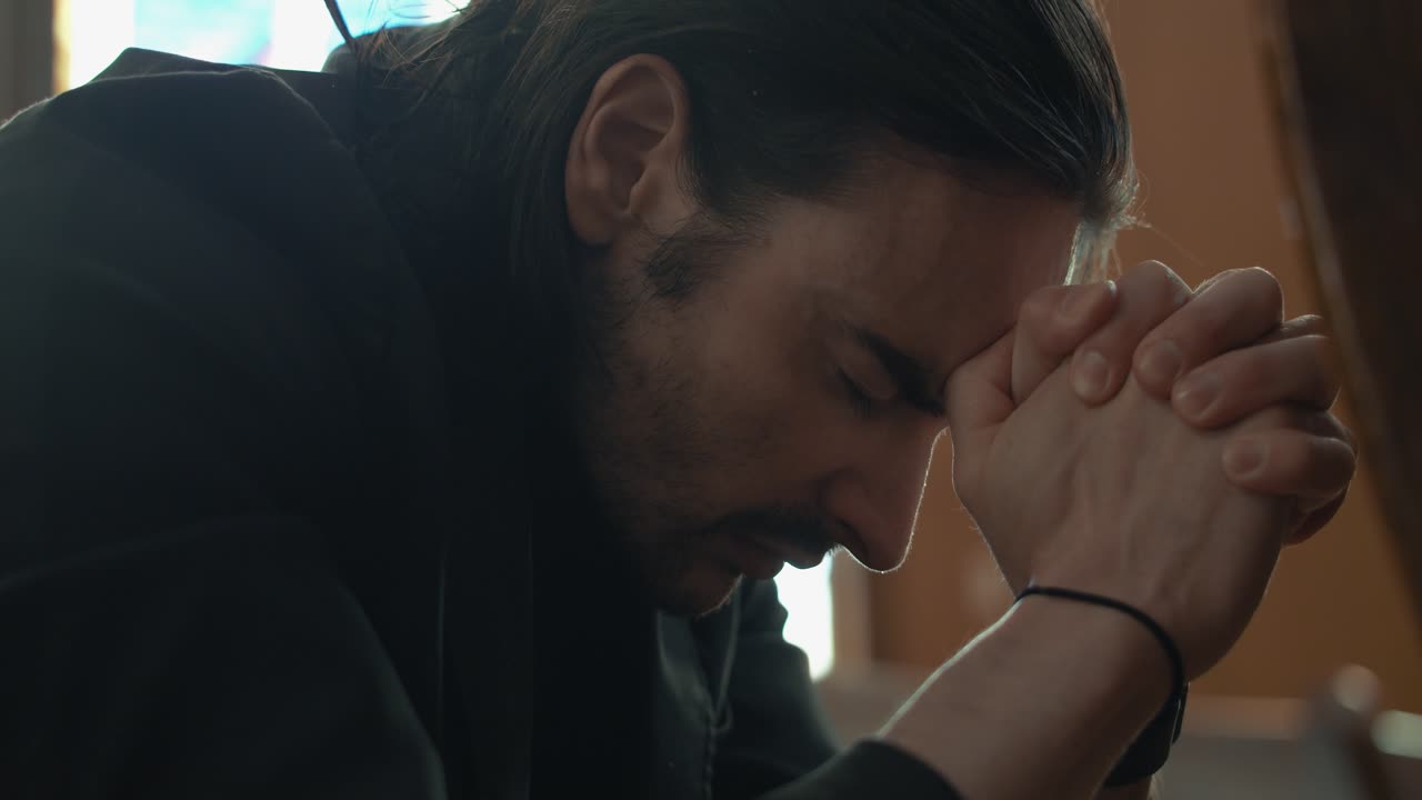 Young man in black suit praying in church in cinematic slow motion