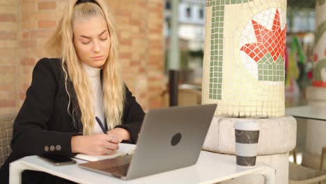 freelancer woman writing notes while working with laptop in cafe