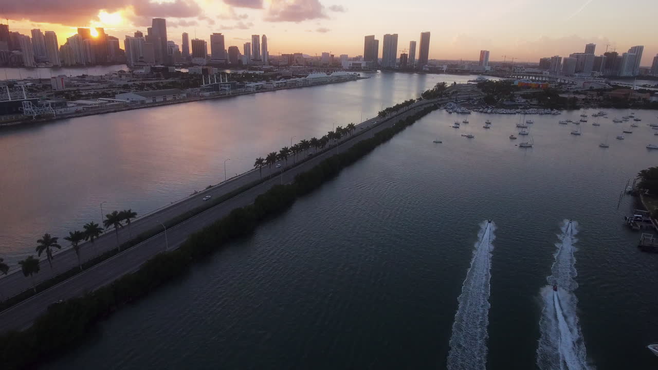 Drone che riprende moto d'acqua nella baia di Miami con palme, ponte e skyline al tramonto