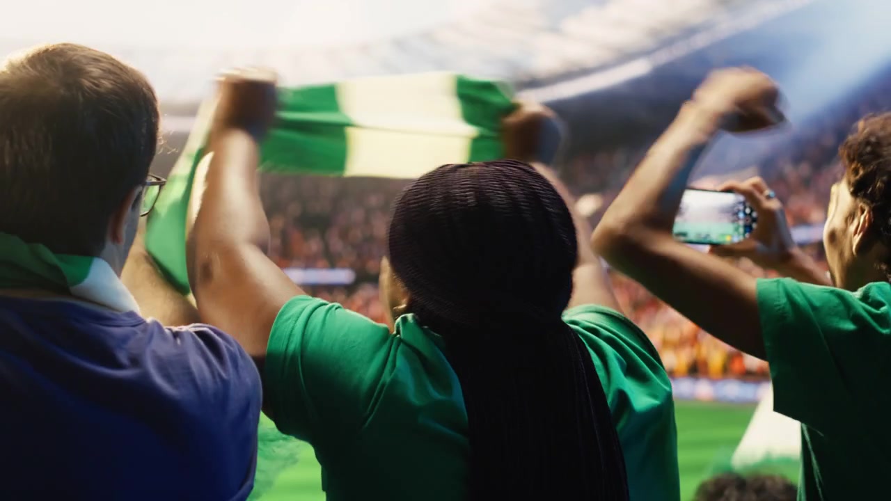 Tifosi di calcio che usano smartphone per registrare una partita giocata su un campo da calcio