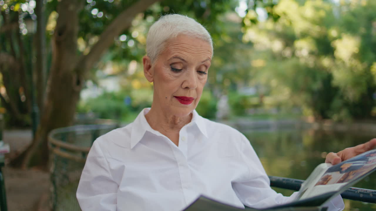 Pensionata legge il giornale al caffè del parco, primo piano. Elegante signora matura si riposa all'aperto.