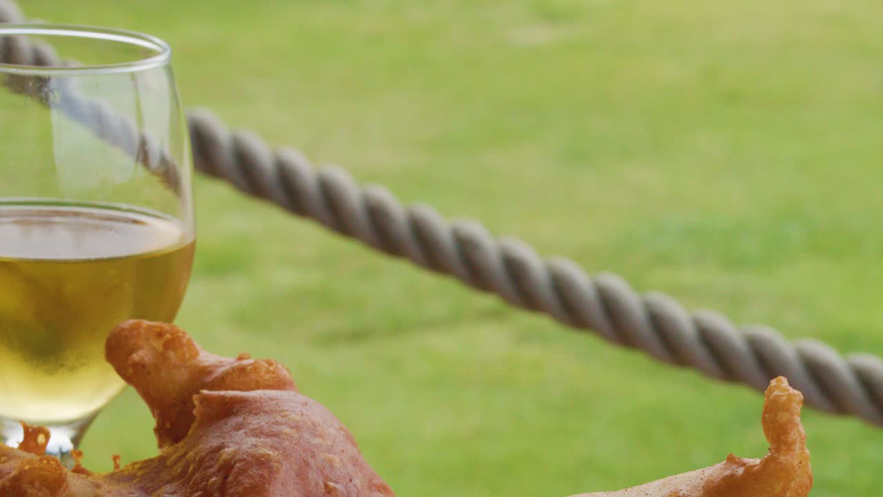Golden beer and crispy fish and chips on outdoor wooden table in daylight