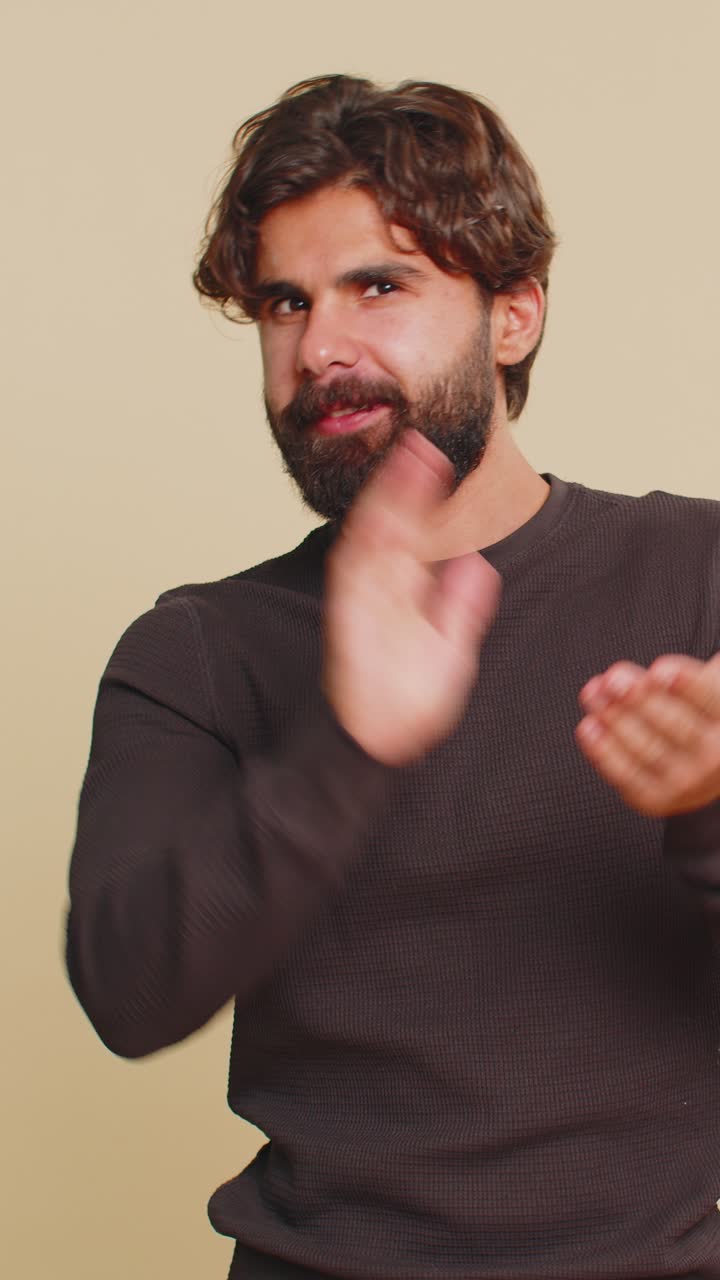 joven libanés mostrando los pulgares hacia arriba y asintiendo con la cabeza en aprobación aplaude las manos contra un fondo beige