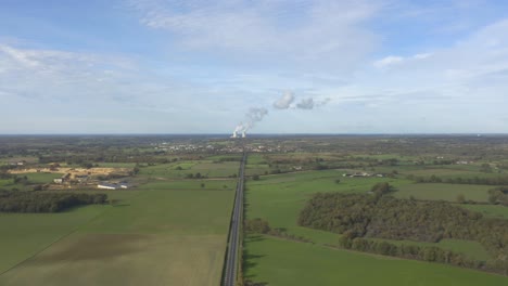 humo blanco que sale de la torre de refrigeración de la planta de energía nuclear - camino entre el campo