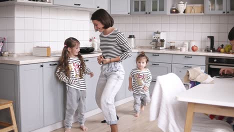 Mother-is-playing-on-the-spatula-like-a-guitar,-two-daughters-are-dancing-nearby