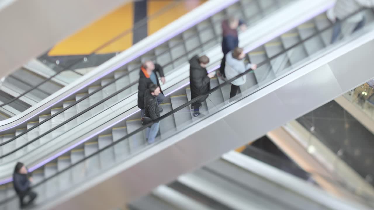Mennesker i bevægelse på rulletrapper i et moderne indkøbscenter. Fotograferet med tilt-shift linse med super lav dybdeskarphed.
