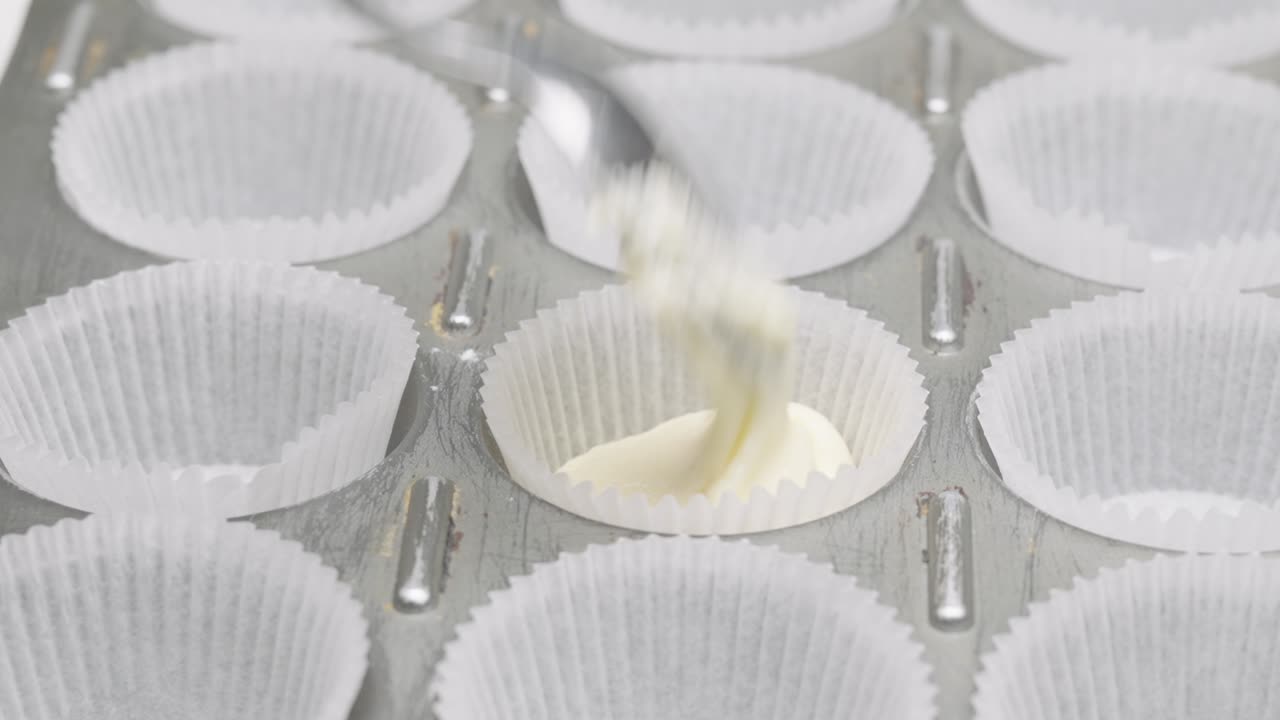Un cucchiaio versa l'impasto della torta in pirottini di carta per cupcake in una teglia da forno, in primo piano.