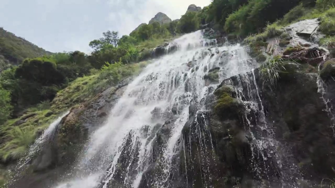 Air terjun sinematik yang perkasa mengalir di atas bebatuan gunung gelap di Ngarai Lompat Harimau (Tiger Leaping Gorge). Menangkap keindahan alam untuk konsep perjalanan berkelanjutan dan kesehatan