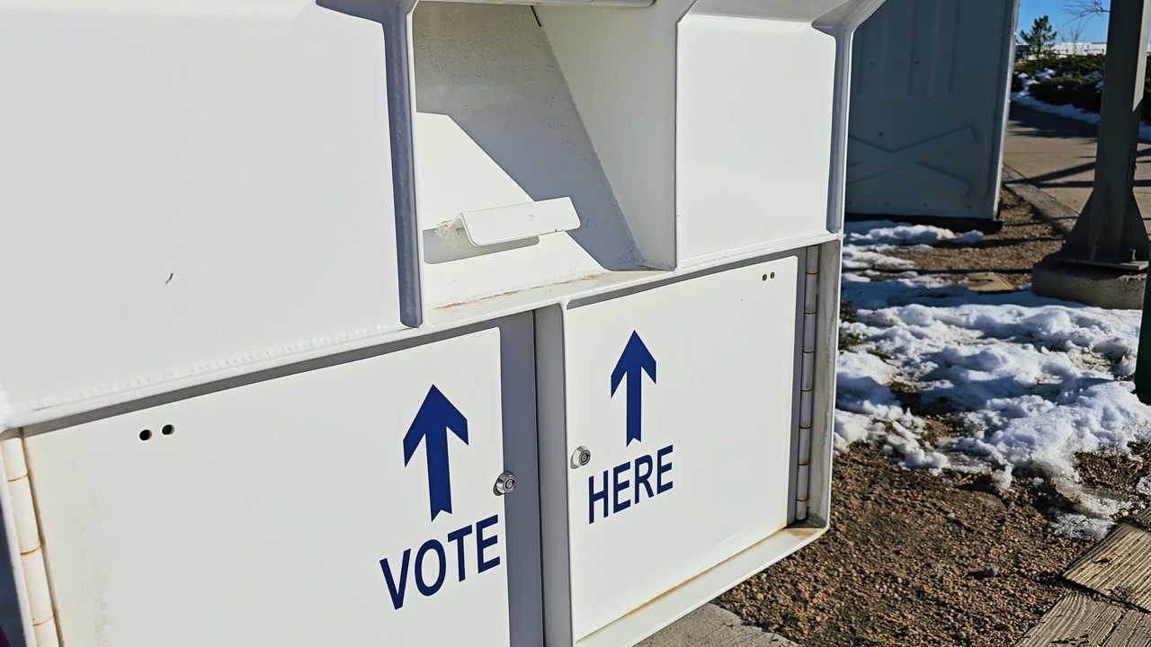 White ballot drop-off box for mail-in election voting displays Vote Here arrows, secure collection compartments, warning notices, and a Voting Closed sign at a snowy outdoor polling site.