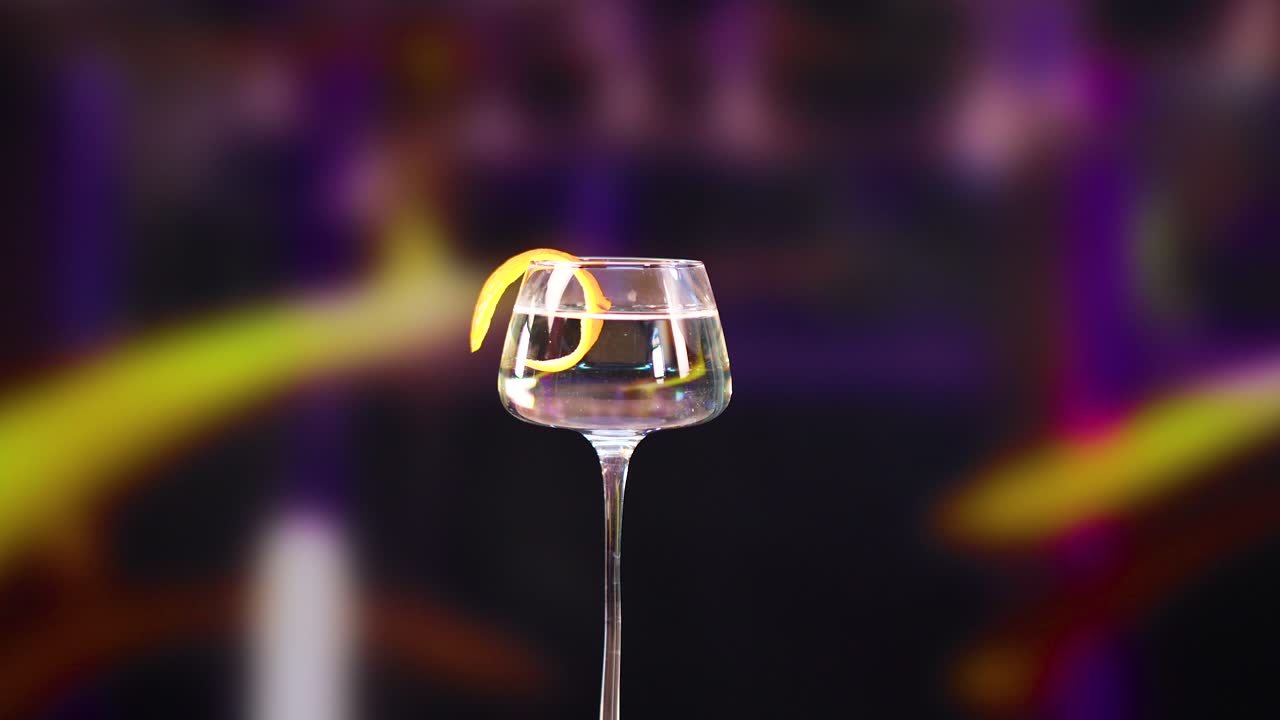 A martini glass with a lemon twist rotates against a vibrant, blurred background with dynamic lighting