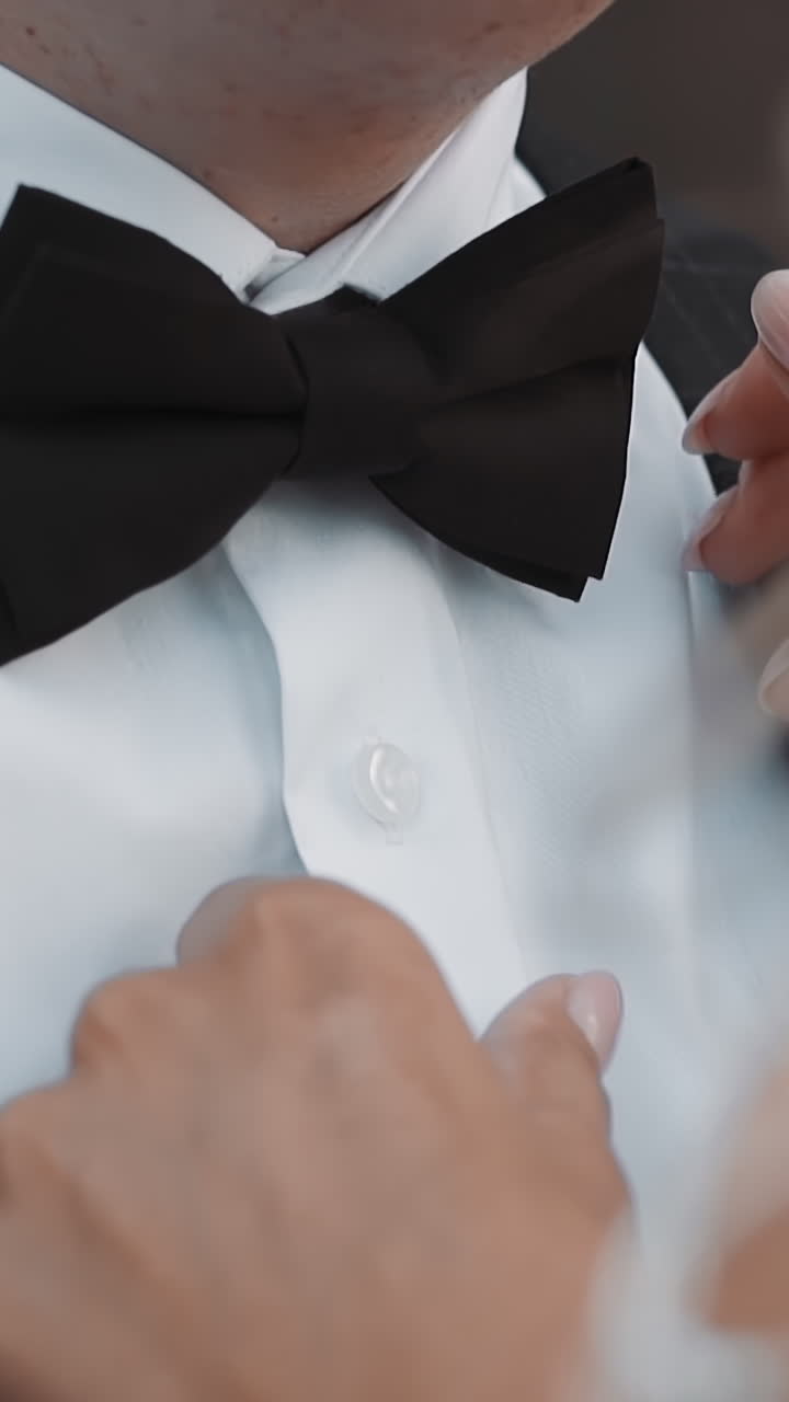 Careful bride adjusts bow tie on neck of young groom at wedding ceremony closeup slow motion. Happy couple at marriage celebration. Love relationship
