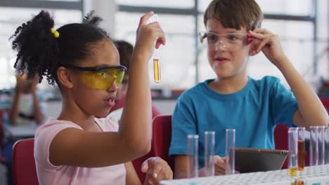 escolares de diversas razas con gafas protectoras sosteniendo un tubo de ensayo durante la clase de química