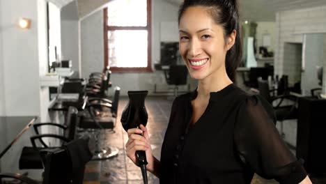 smiling female hairstylist holding hair dryer in hair salon