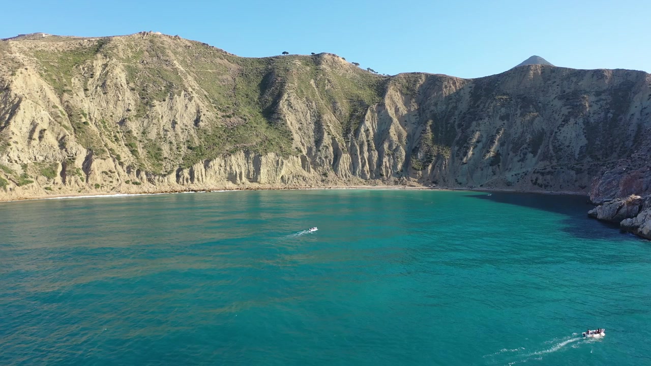 Vista aérea panorámica que revela una espectacular bahía costera con aguas turquesas, playas aisladas y escarpados acantilados montañosos a lo largo de la costa mediterránea marroquí.
