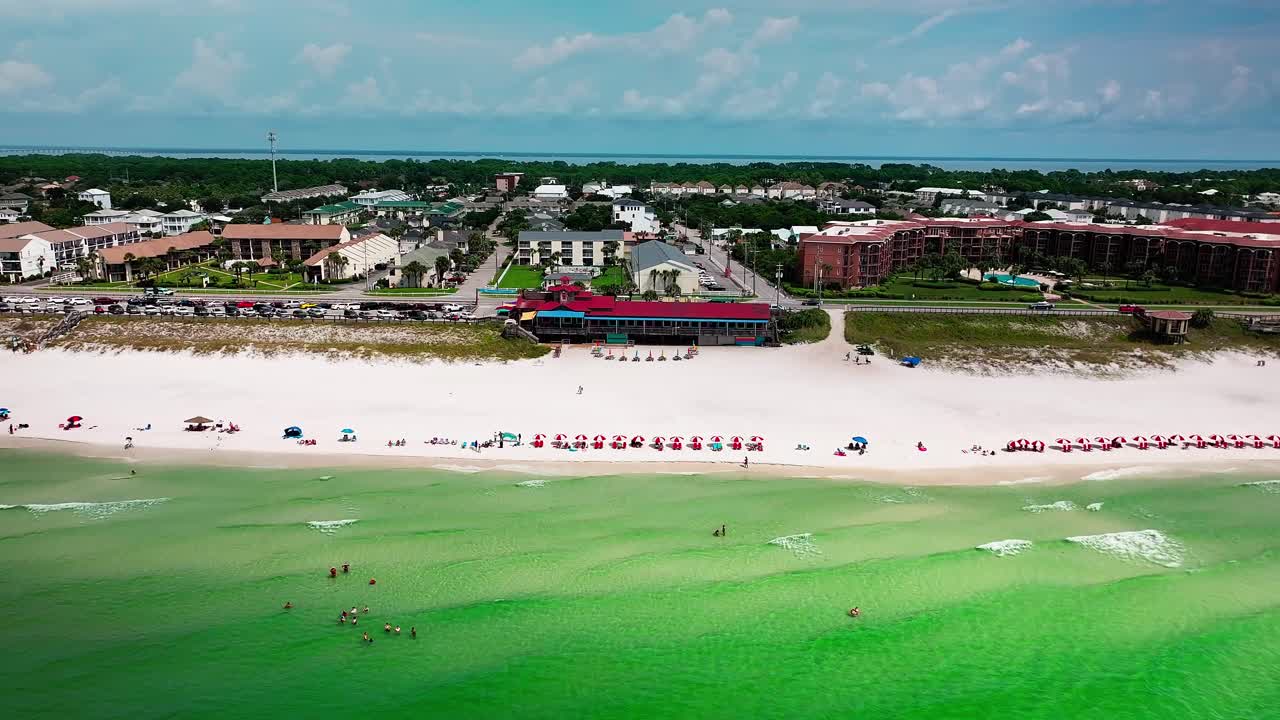 Drone aerial view flying towards from Pompano Joe's restaurant in Destin Florida with a view of old 98, white sand, emerald green water and lots of umbrellas and beach chairs in Destin Florida