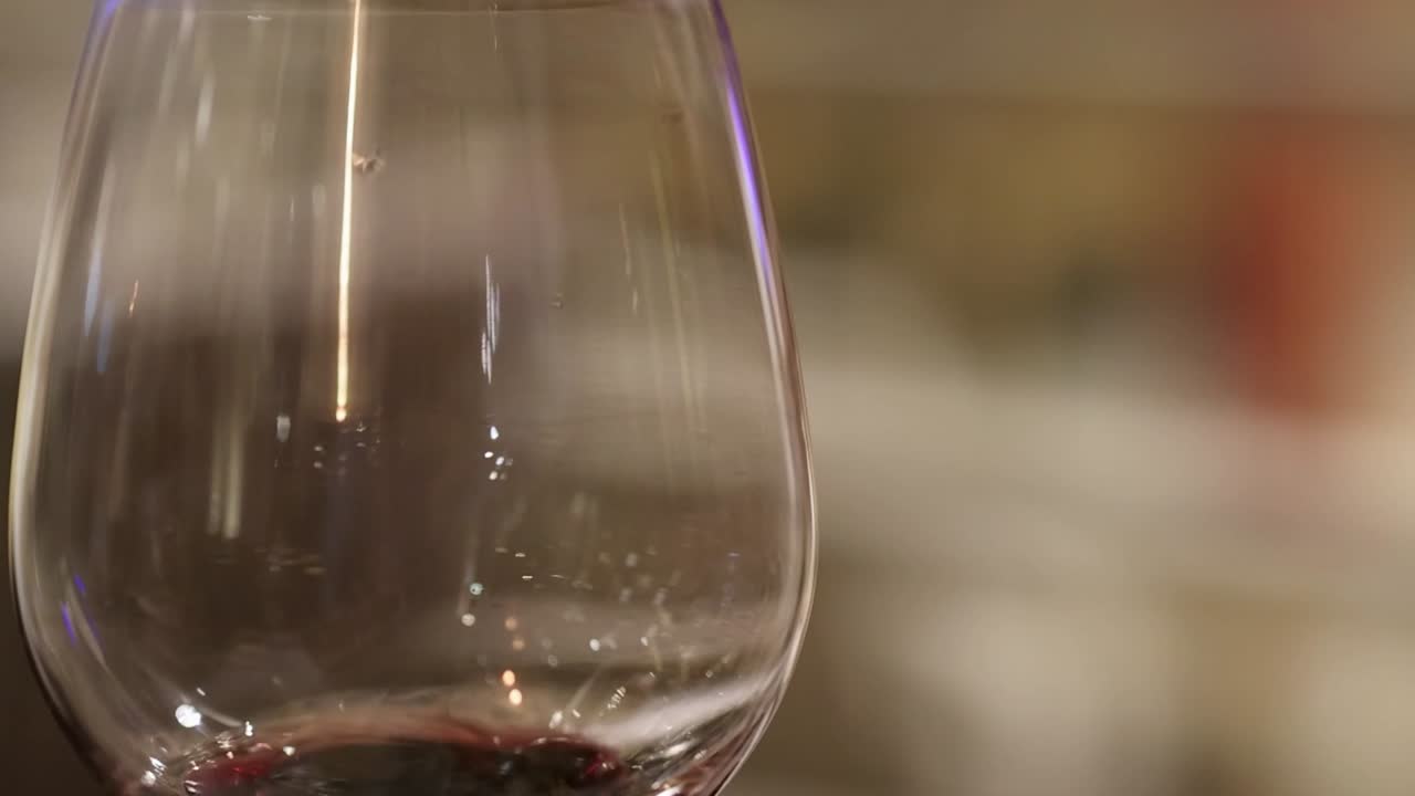A detailed view of red wine droplets forming in a glass, showcasing the liquid's movement and texture.