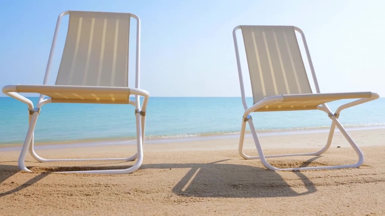 Strandstole står stille på stranden, med sand og hav. De er lavet med trælameller og metaltekstur, set fra øjenhøjde, med blå og sandfarvede accenter, der skaber en afslappet stemning og viser klare detaljer.