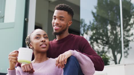 happy african american couple embracing and relaxing with coffee outside house