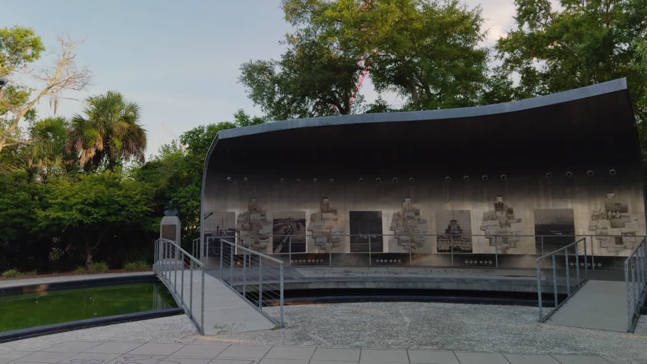 Slow-motion pan of North Charleston's Riverfront Park Naval Base Memorial. Filmed at 60fps, slowed to 24fps. Features the memorial, trees, and calm water. A historical monument in a peaceful park