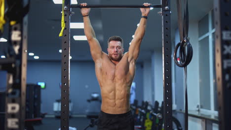 shirtless man training on a crossbar. portrait of a professional athlete doing exercise with tightening his legs in the gym. everyday workout routine.