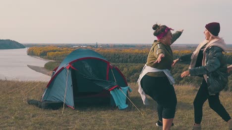 pudgy-lady-runs-to-girl-friends-and-hugs-near-blue-camp-tent