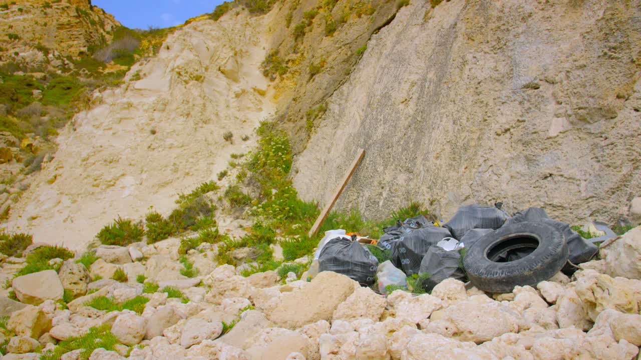 Environmental Issue. Bags Of Garbage And Old Rubber Tire Dumped On Rocky Mountainside. wide shot