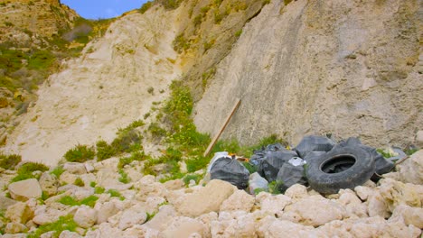 environmental issue. bags of garbage and old rubber tire dumped on rocky mountainside. wide shot