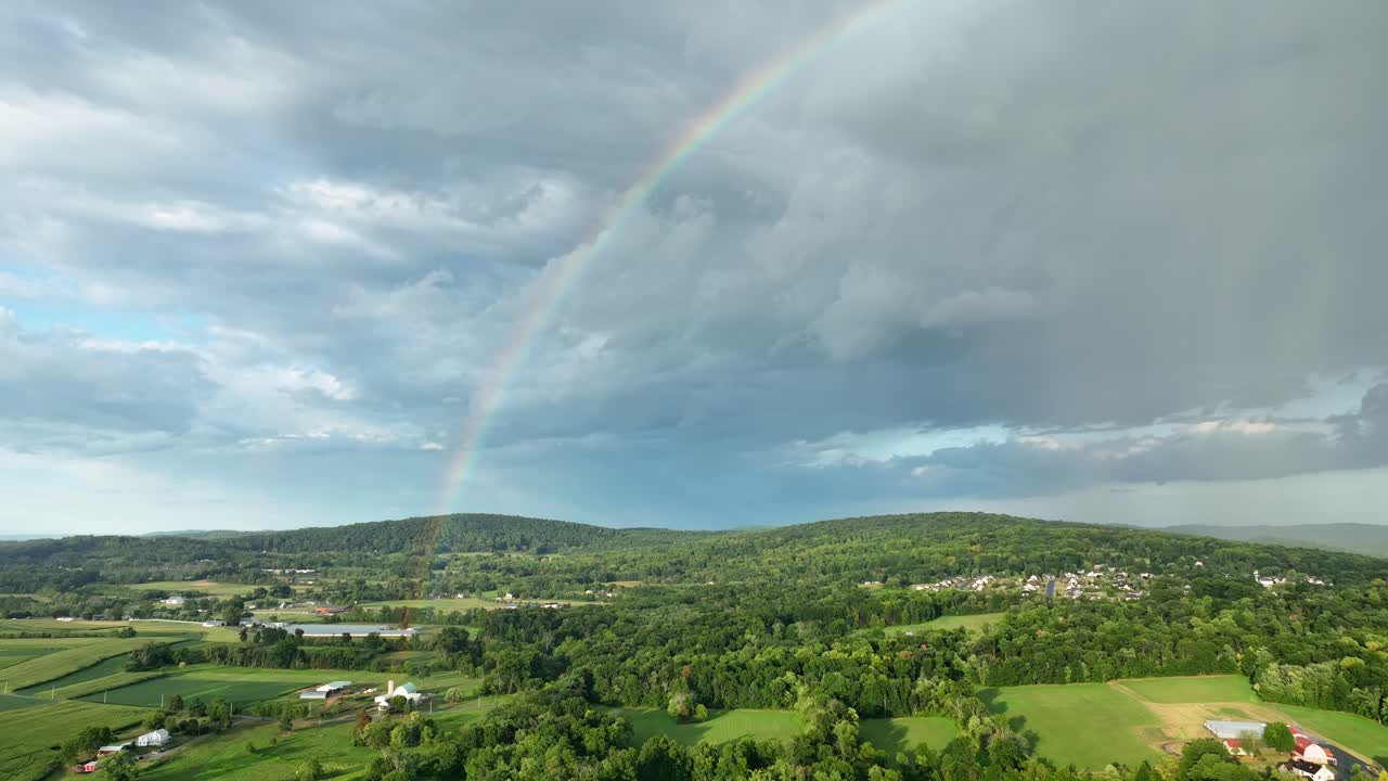 un vuelo aéreo sobre las tierras de cultivo rurales verdes después de una tormenta con las nubes y un arco iris en el cielo
