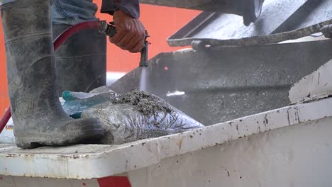 Un-Trabajador-En-Un-Sitio-De-Construcción-Limpiando-Una-Bolsa-De-Cemento-Con-Una-Manguera-De-Agua