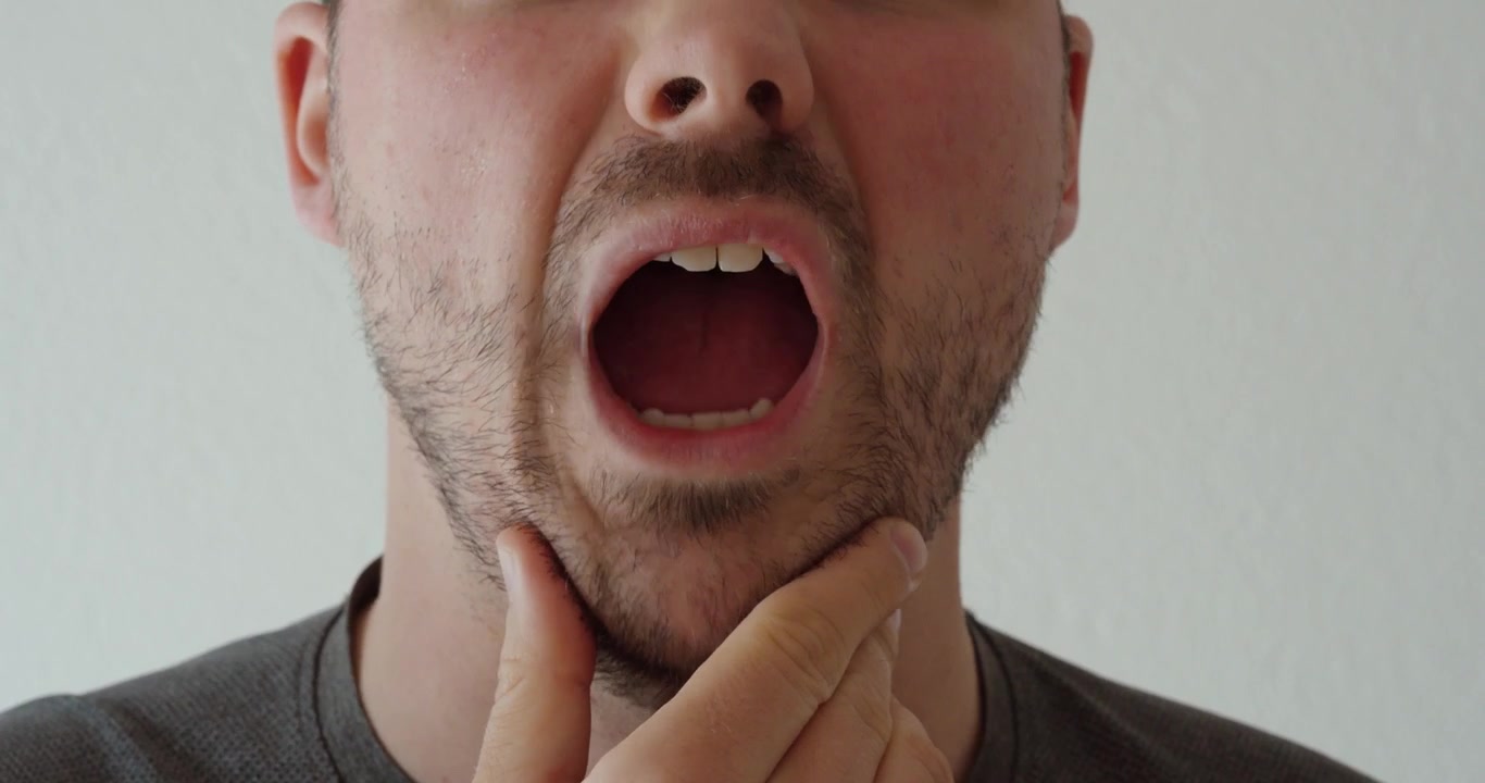 Uomo che si tocca la mascella e il viso mentre prova disagio nella zona della mascella. Adatto per problemi dentali, tensione mascellare, disturbi dell'ATM, mal di denti e concetti sanitari