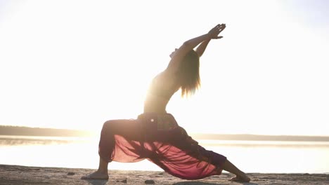 vista lateral de una joven atractiva practicando yoga en la postura de guerrero virabhadrasana en la orilla del mar. bruma ligera del sol