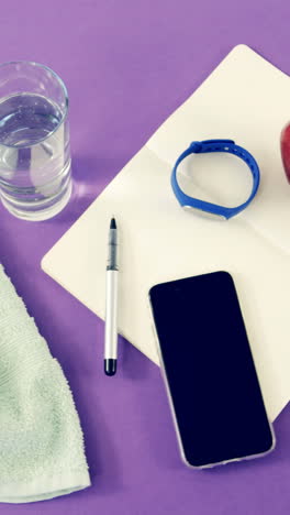teléfono móvil, servilleta, agua, manzana, cuaderno, bolígrafo y banda de fitness