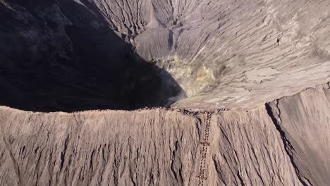 Aerial-top-down-shot-of-burning-crater-of-Bromo-Volcano-during-sunny-day-in-Indonesia---backwards-tilt-up-shot-in-tengger-semeru-nationalpark