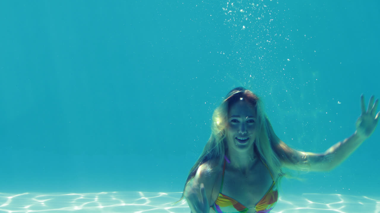 행복한 금발이 수영장에 뛰어들고 손을 흔들고