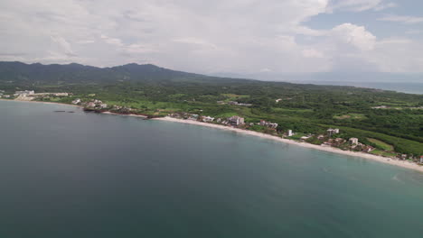 Drone-moves-forward,-approaching-the-beach-from-the-ocean,-showcasing-mountains-and-the-coastline