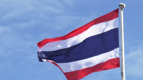 waving the kingdom of thailand flag on a pole with blue sky and white clouds in the background