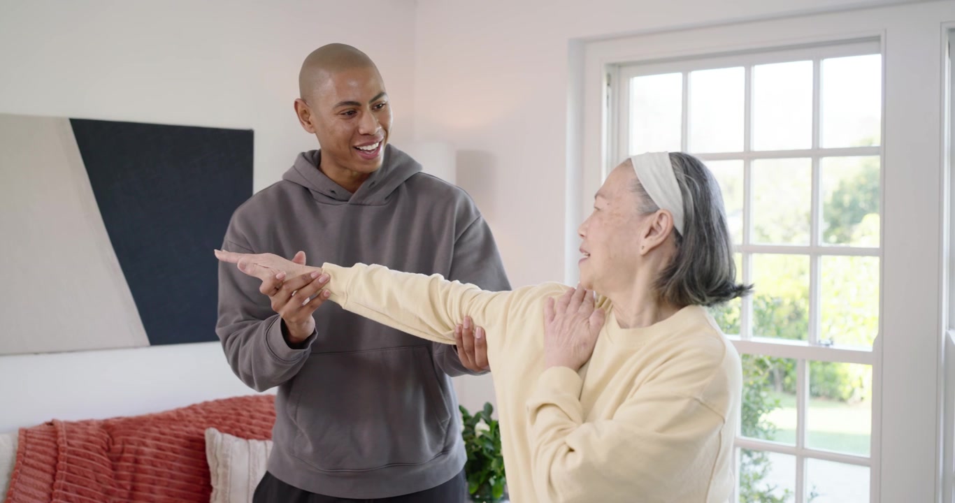 African American man holding arm, assisting mobility for Asian senior woman at home window
